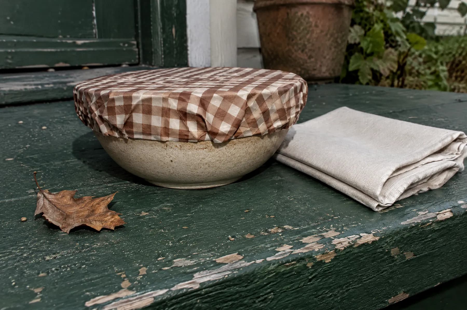 A stoneware bowl covered with a gingham beeswax wrap on a green porch step